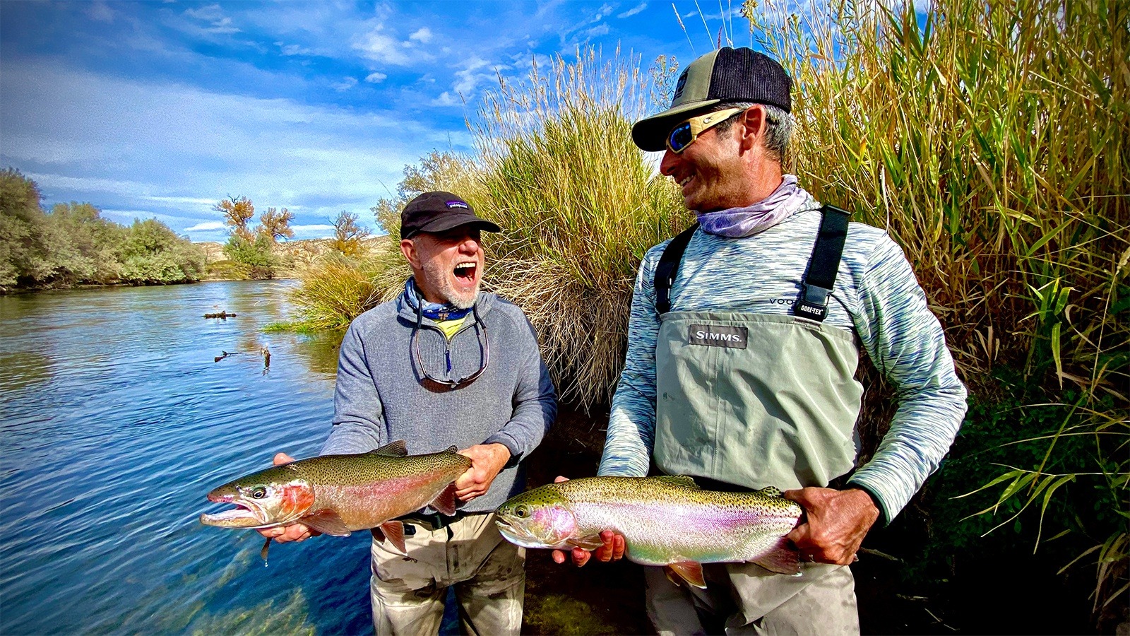 Two men posing with their catch. One, who is holding a cut throat, is laughing hysterically.