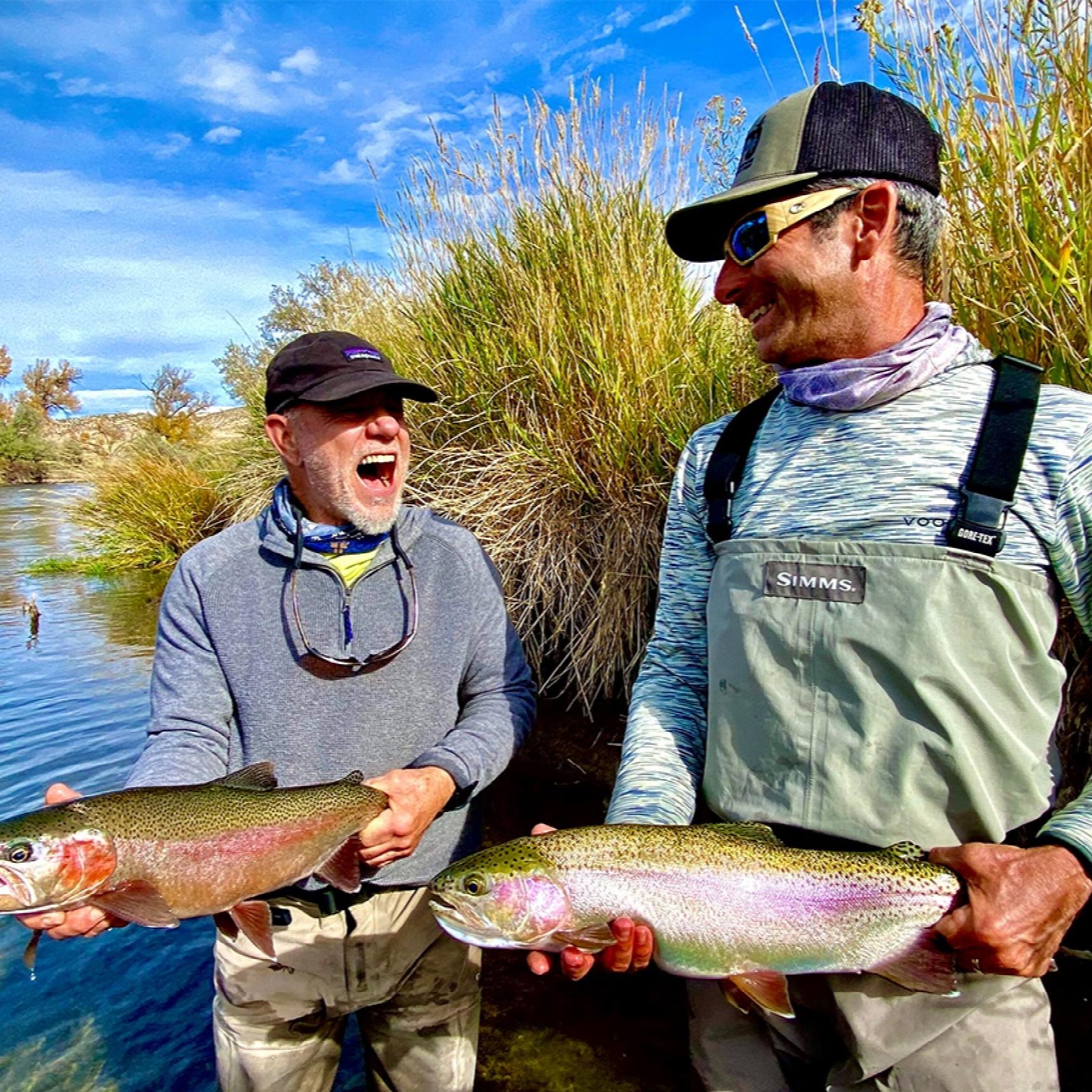 Two men posing with their catch. One, who is holding a cut throat, is laughing hysterically.