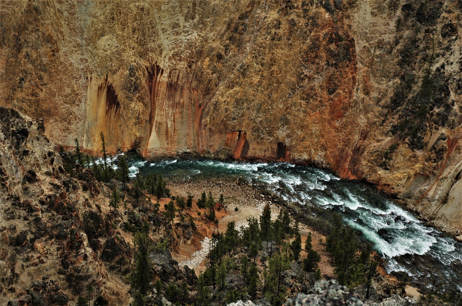 Aerial view of a whitewater river with a slight curve to the left at the bottom of a deep, steep canyon