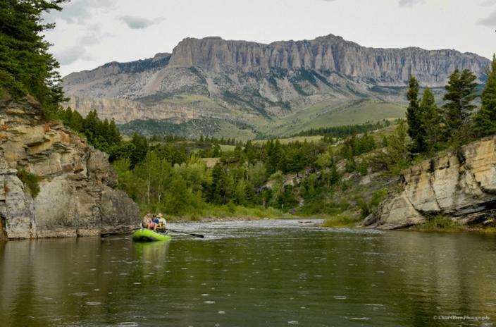Green raft floating on river with Rocky Mountains in the background